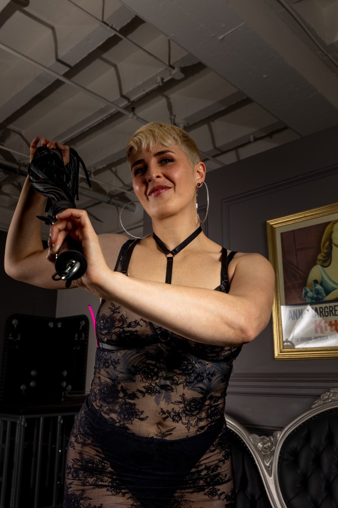 Queen Emma smiles as she holds a flogger ready to strike